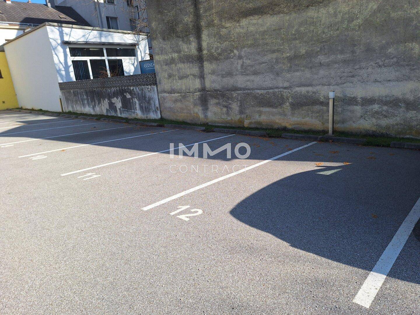 Asphaltierter Parkplatz mit deutlich nummerierten Stellplätzen und einer angrenzenden Mauer.