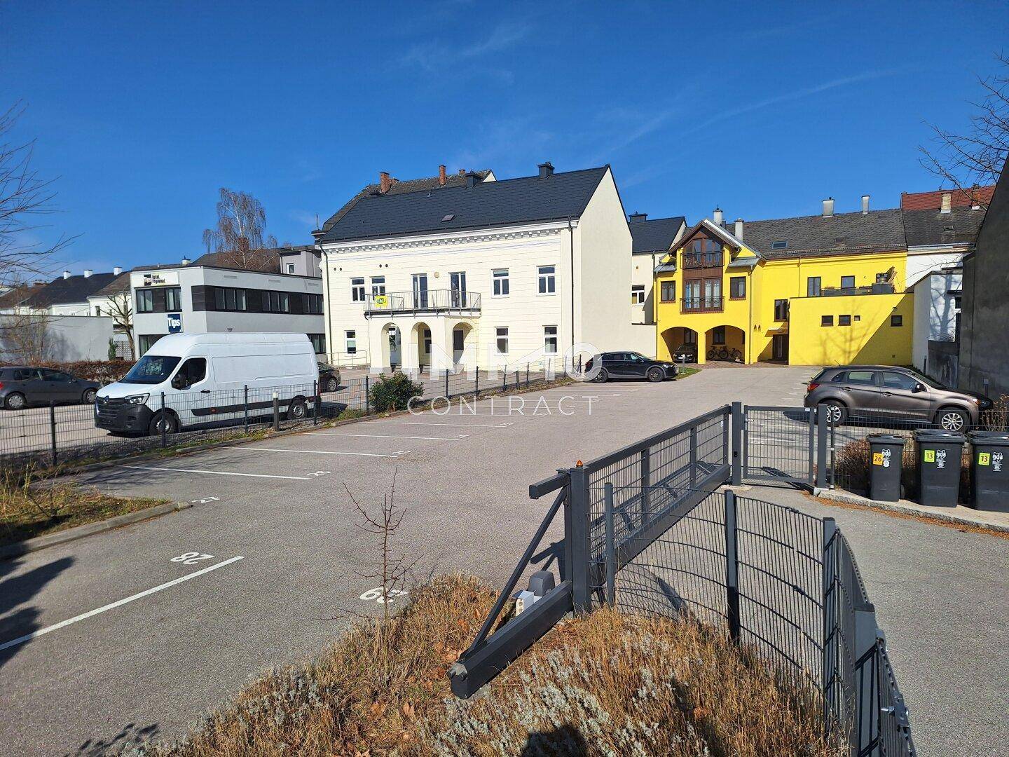 Großer Außenparkplatz mit verschiedenen Gebäuden im Hintergrund und einer Abfahrt zu einer Tiefgarage.