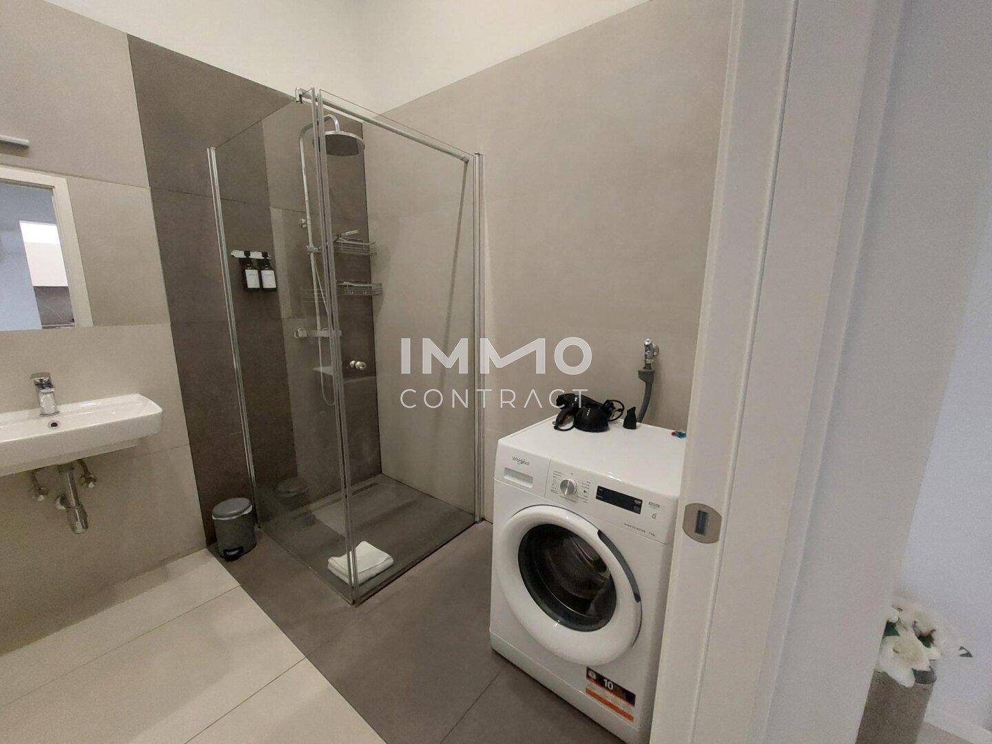 Modernes Badezimmer mit ebenerdiger Dusche, Waschbecken und einer praktischen Waschmaschine.