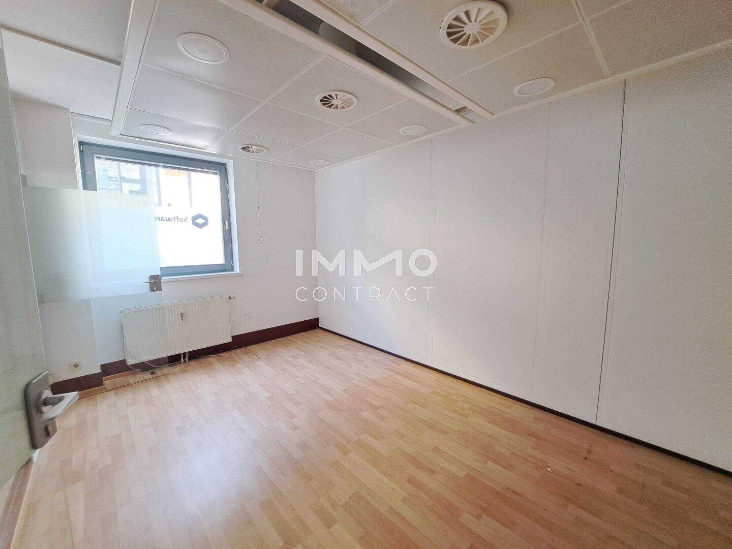 Einzelbüro mit Holzfußboden, einem Fenster und einer abgehängten Decke mit integrierter Beleuchtung und Lüftung.