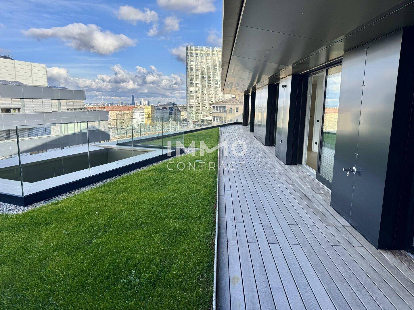 Weitläufige Dachterrasse mit Rasenfläche, Holzdeck und Blick auf die Skyline der Stadt.