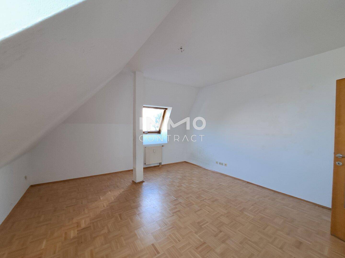 Geräumiges Dachgeschosszimmer mit Parkettboden, Dachfenster und Heizkörper.