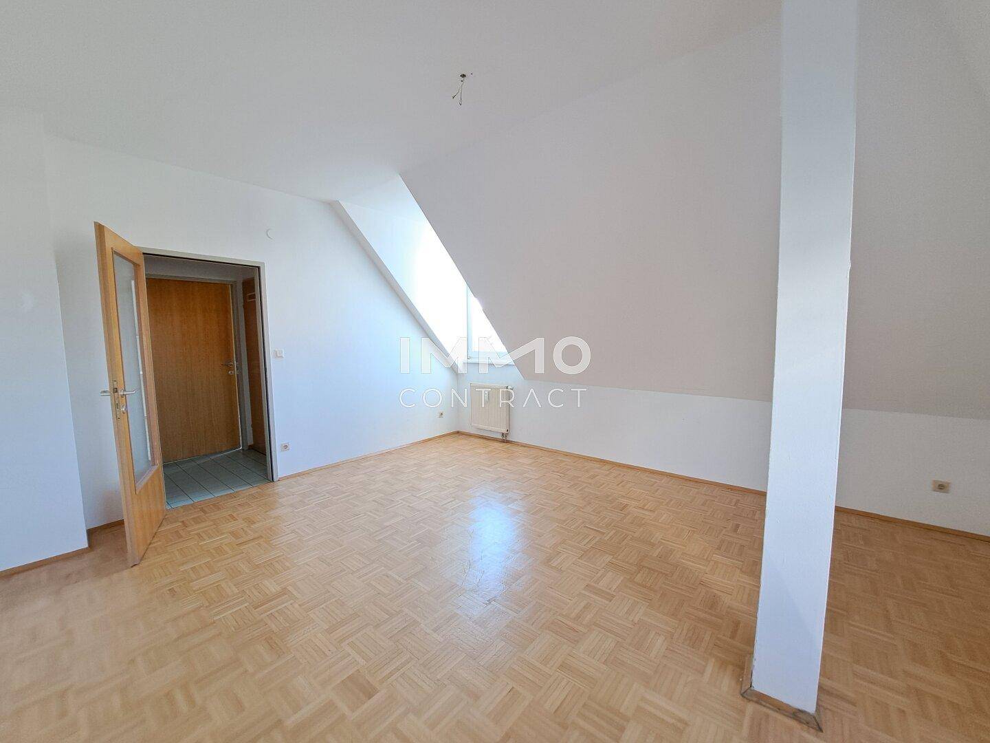 Helles Zimmer im Dachgeschoss mit Parkettboden und schräger Decke.