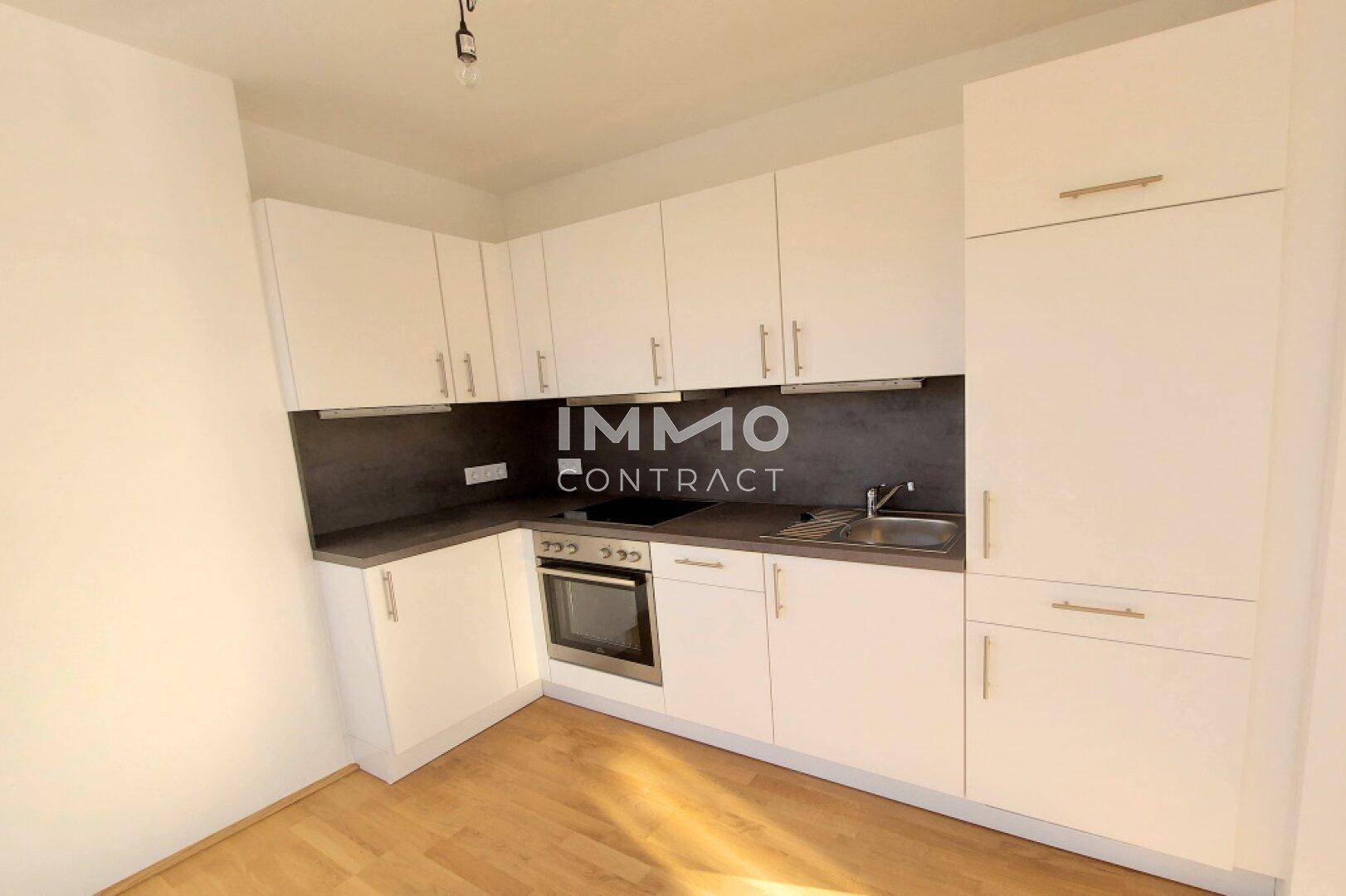 Funktionale Einbauküche mit weißen Schränken, dunkler Arbeitsplatte und integrierten Geräten.