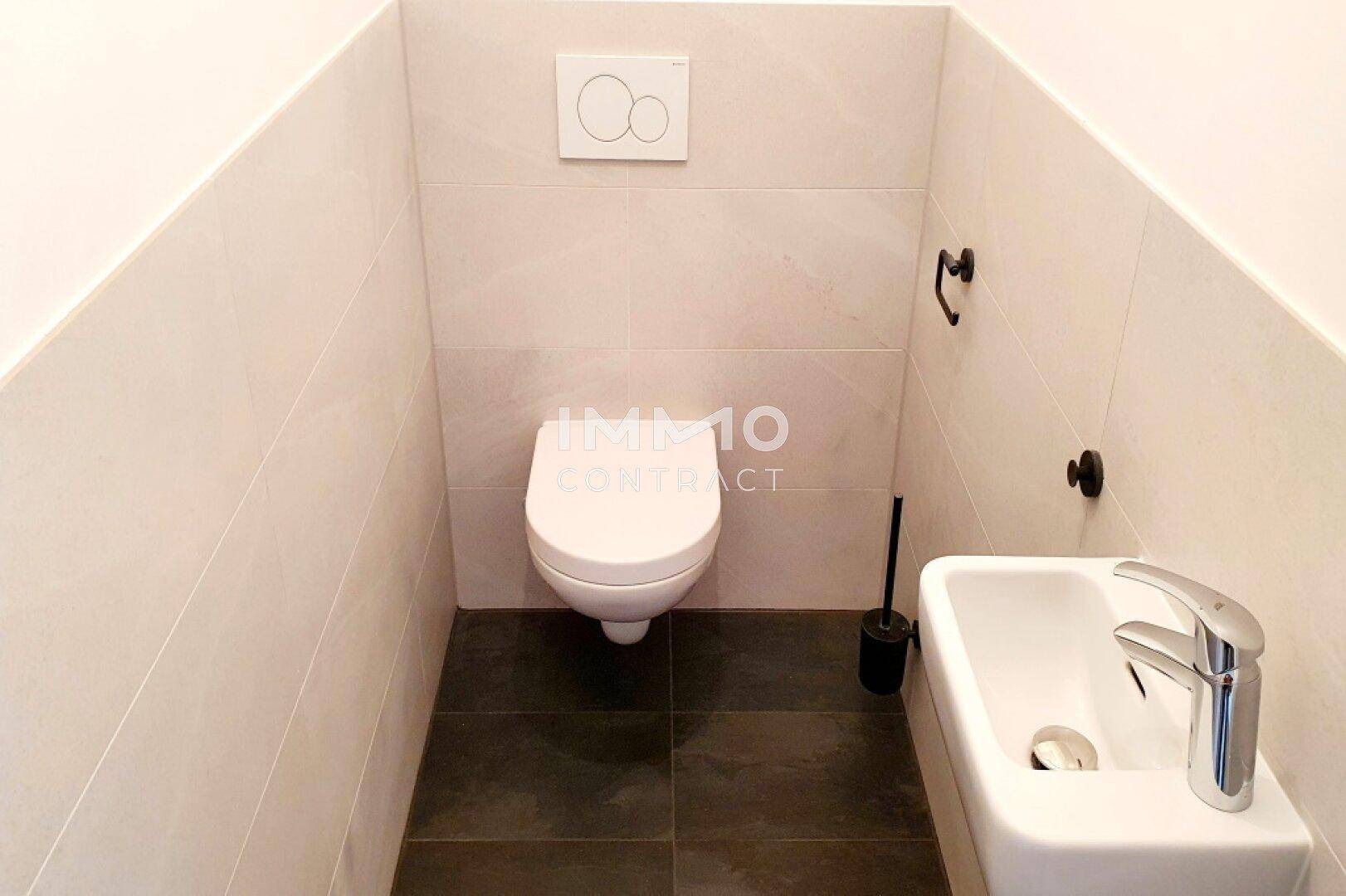 Modernes Gäste-WC mit wandhängender Toilette, kleinem Waschbecken und dunklen Bodenfliesen.