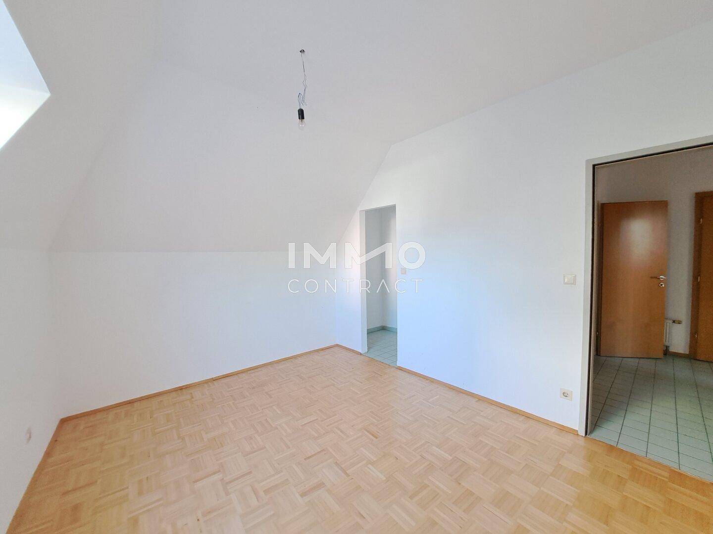 Dachgeschosszimmer mit Parkettboden und Zugang zu weiteren Räumen.