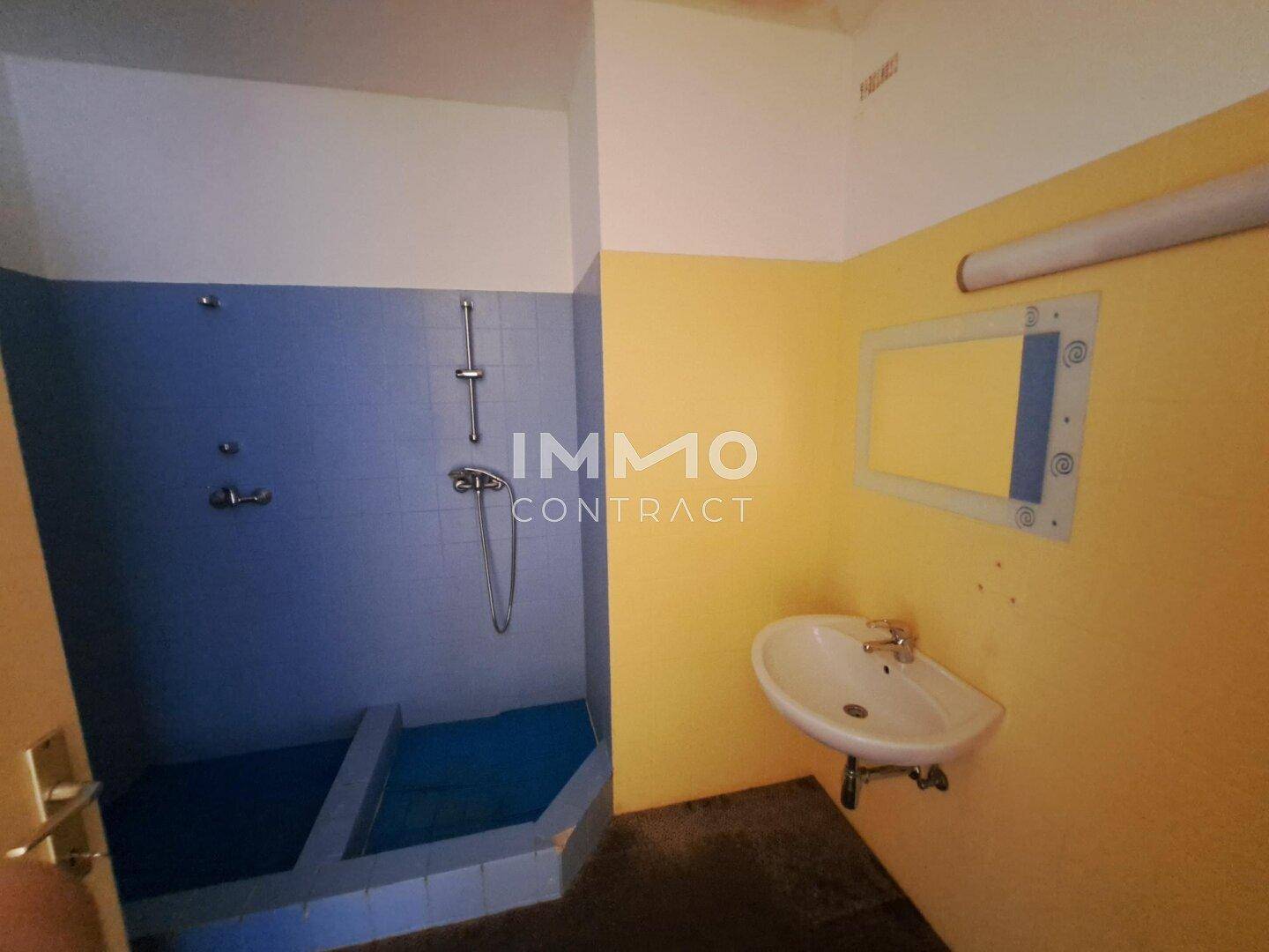 Badezimmer mit Duschbereich, Waschbecken und farbigen Fliesen an den Wänden in Gelb und Blau.