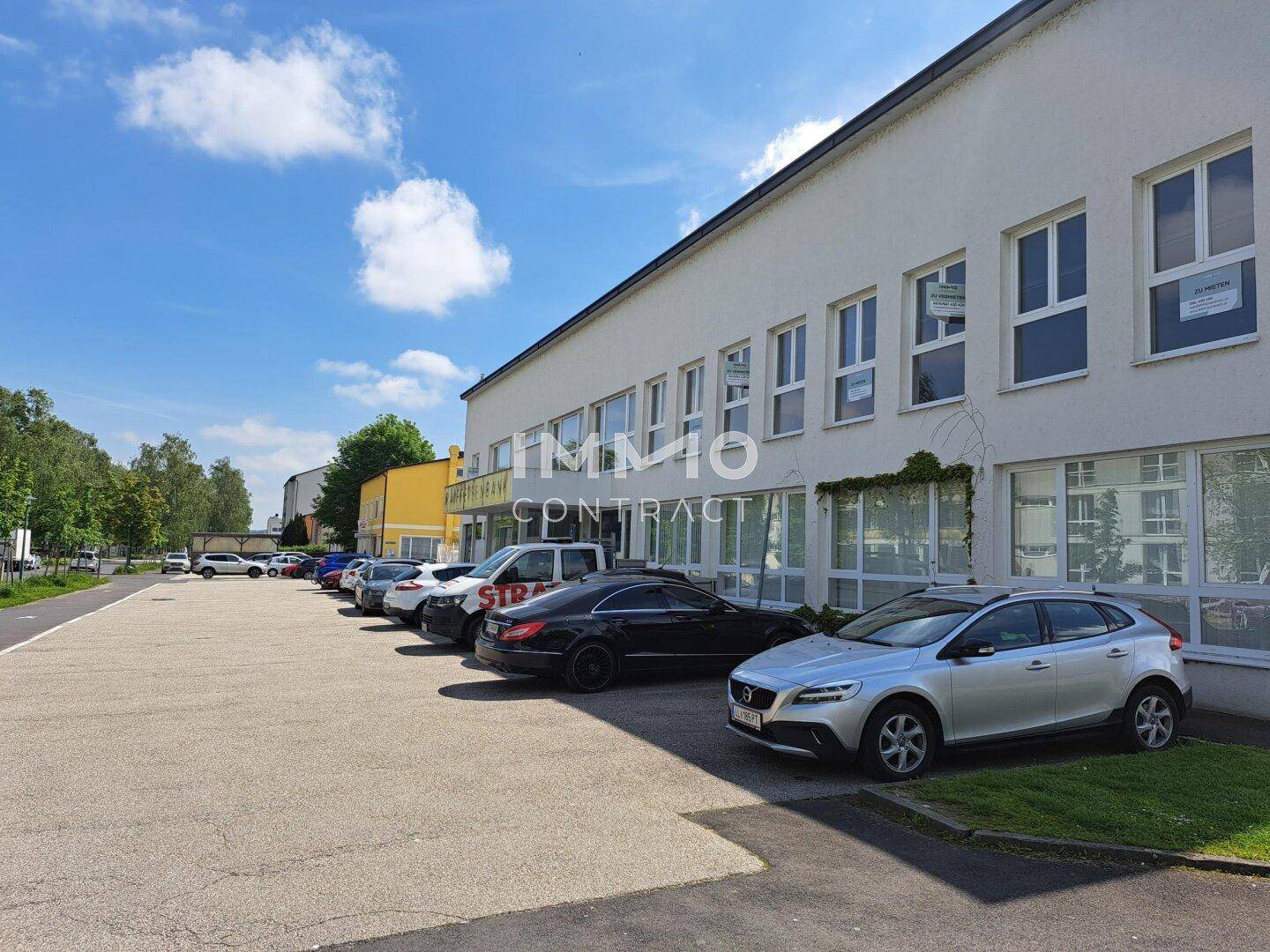 Außenansicht eines Geschäftsgebäudes mit Parkplätzen und Autos unter blauem Himmel.