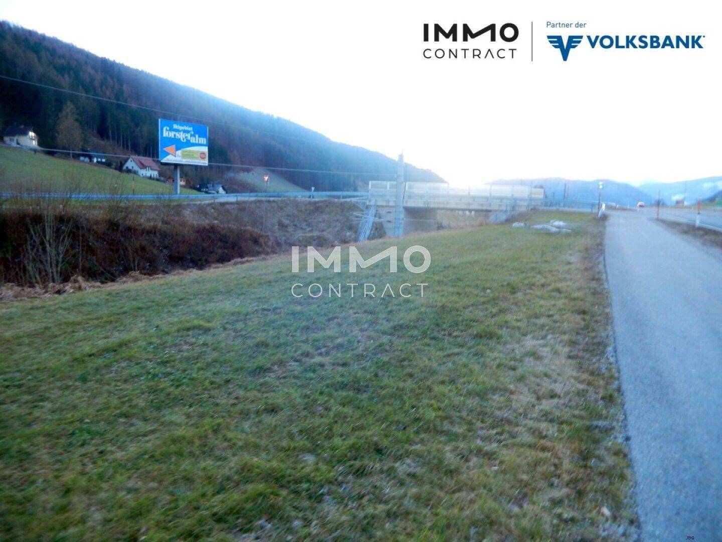 Grünfläche neben einer Straße mit einer Brücke und einer Werbetafel im Hintergrund der Landschaft.