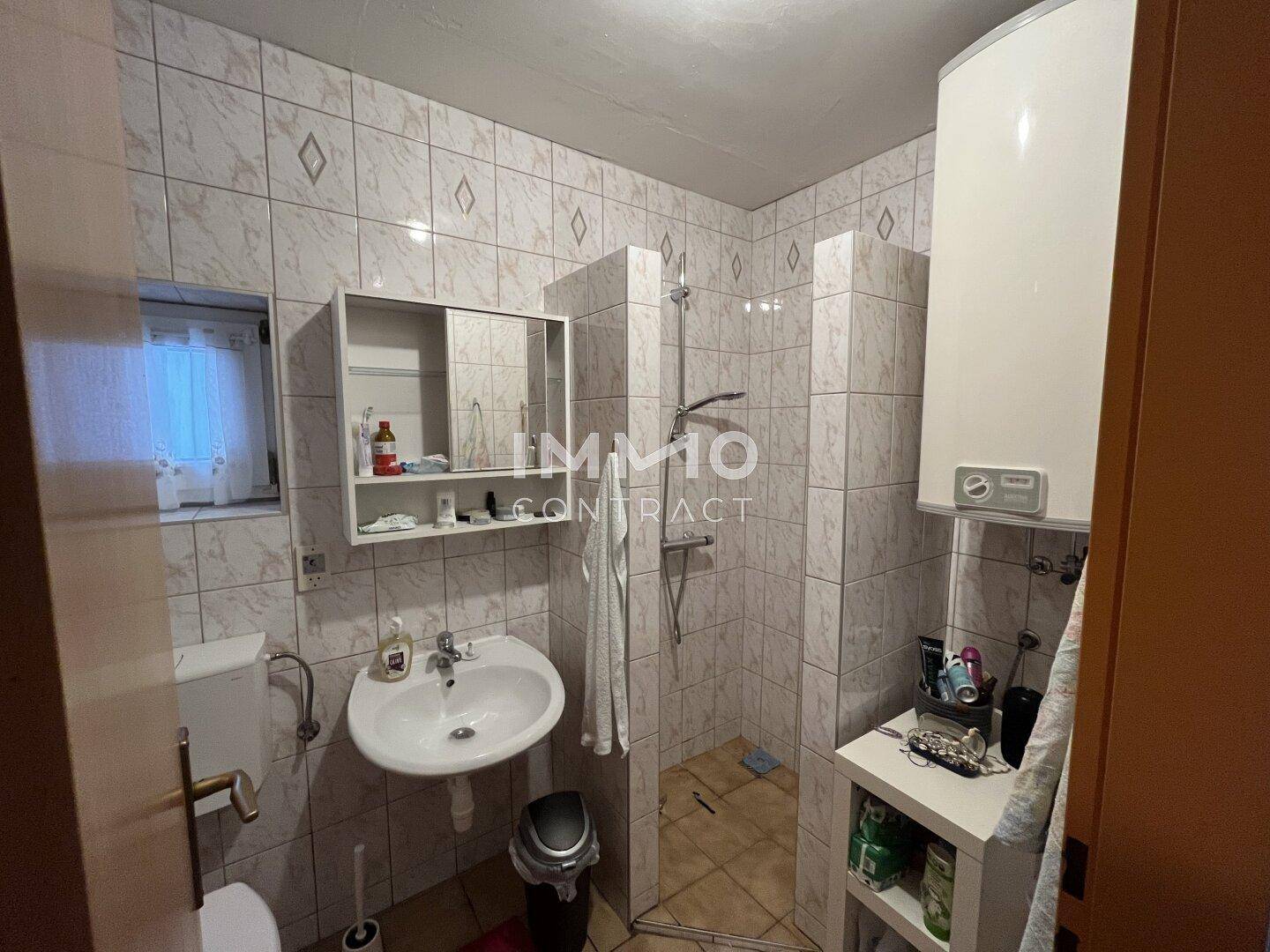Gefliestes Badezimmer mit Dusche, Waschbecken, Toilette und einem Warmwasserboiler.