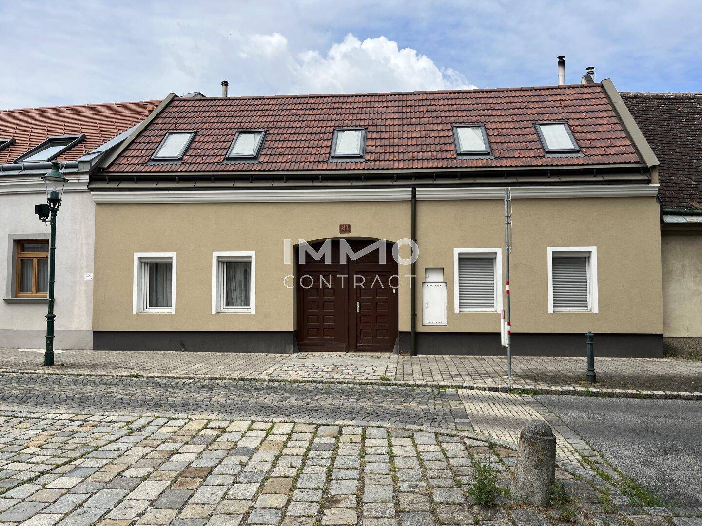 Traditionelles Gebäude mit Satteldach, Dachfenstern und einer hellen Fassade an einer Kopfsteinpflasterstraße.
