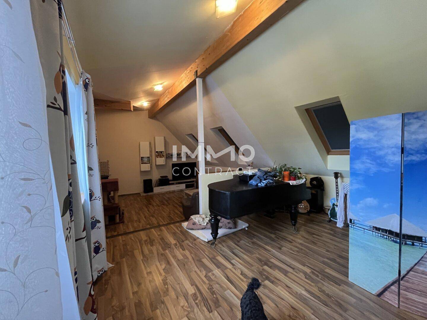 Gemütlicher Wohnbereich im Dachgeschoss mit Holzbalken, Dachfenstern und Laminatboden.