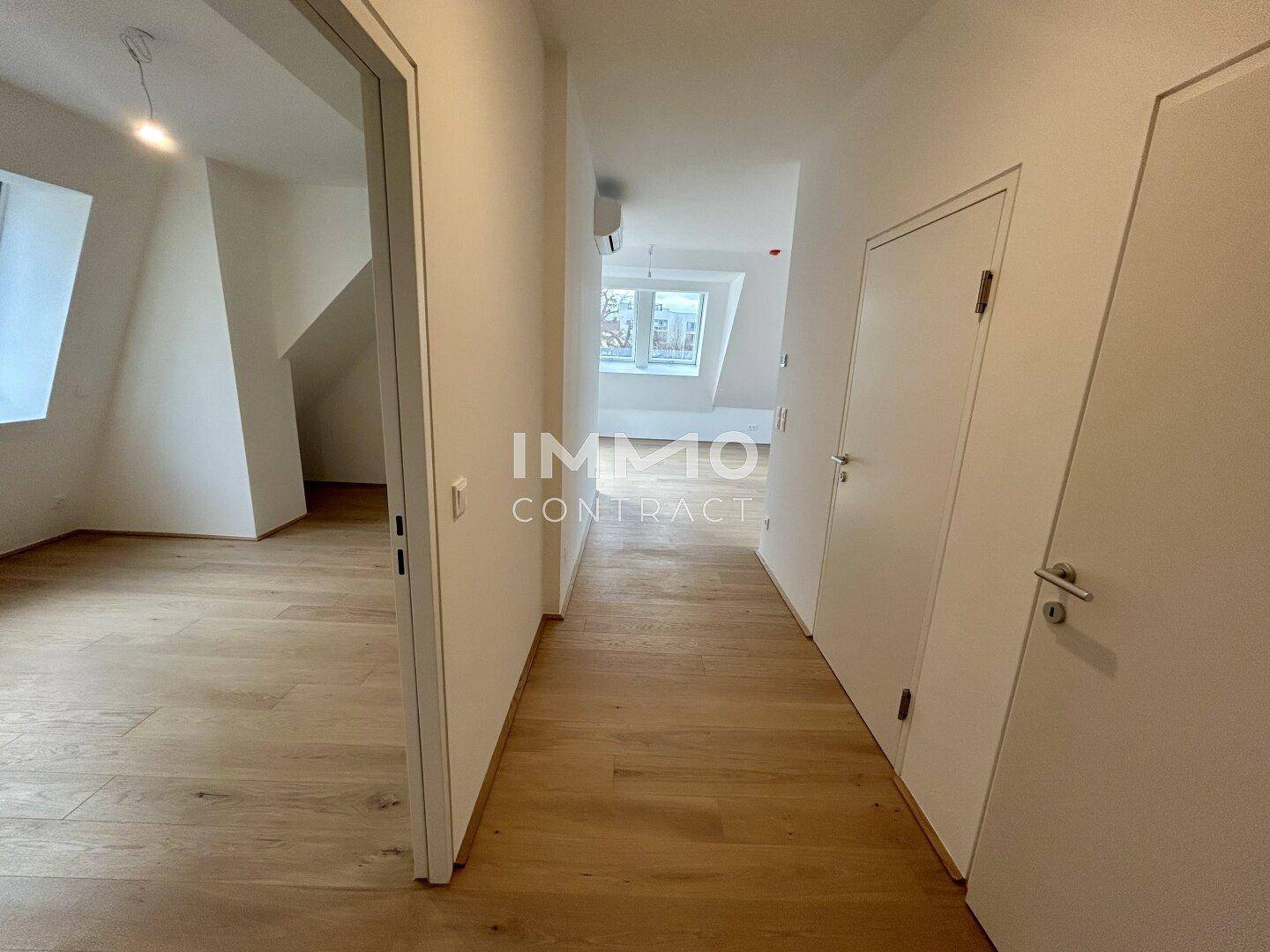 Heller Flur mit Holzboden, weißen Türen und Blick in angrenzende Dachgeschossräume.