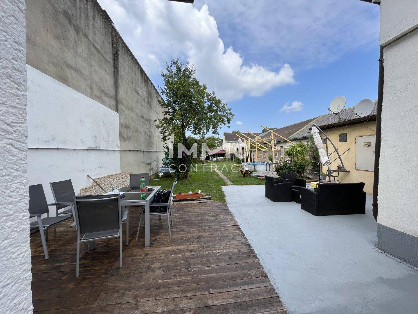 Terrasse mit Holzboden und Sitzgelegenheiten, angrenzend an einen Gartenbereich mit Pool.