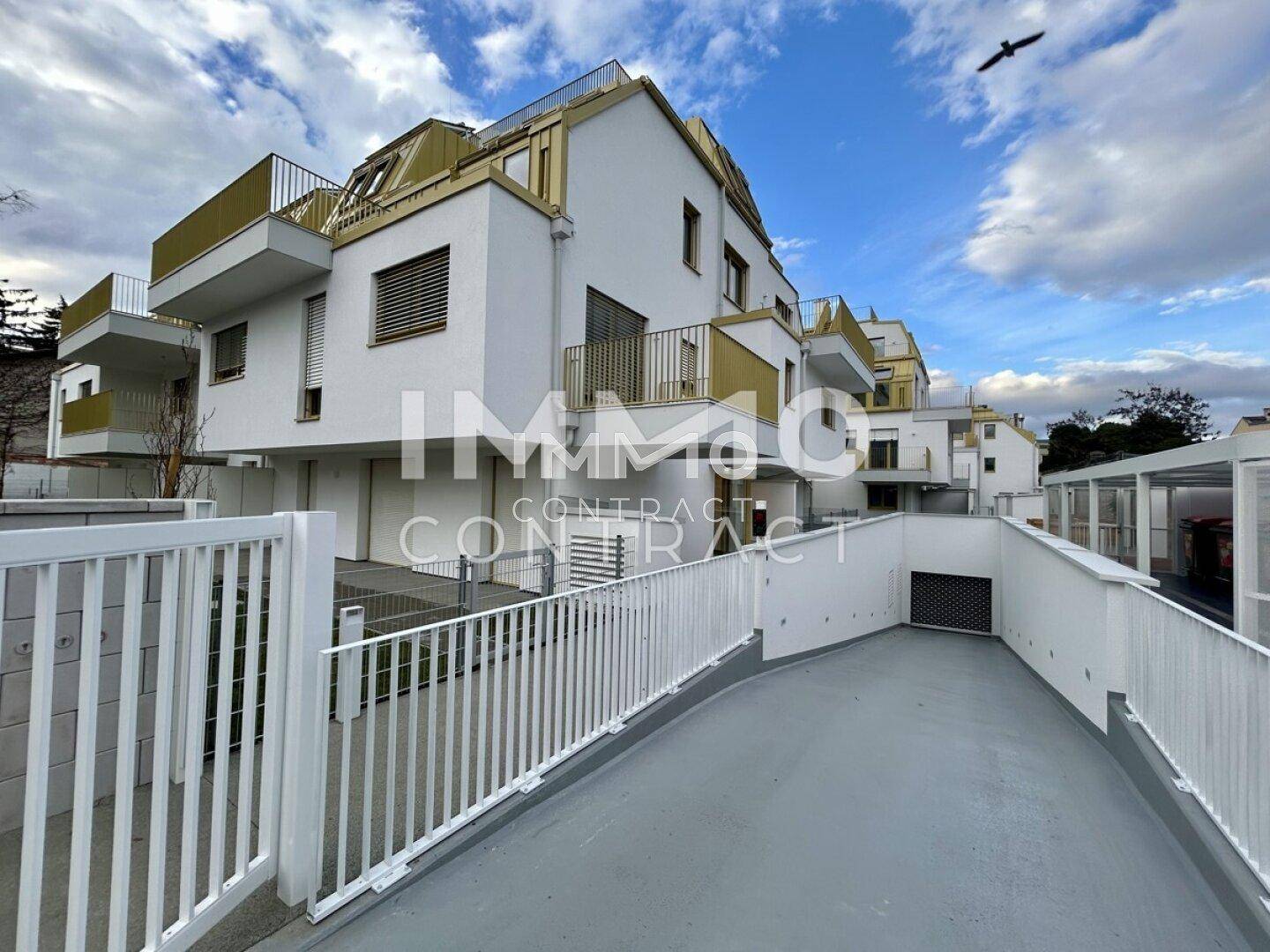 Modernes Mehrfamilienhaus mit Tiefgaragenzufahrt und Balkonen unter bewölktem Himmel.