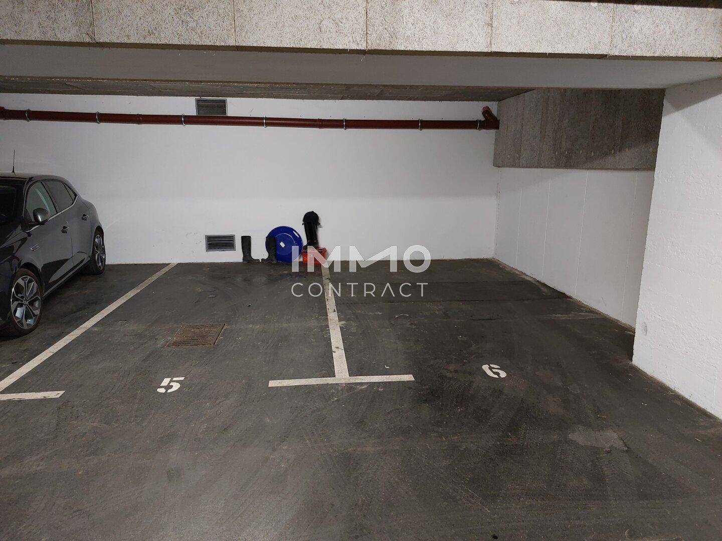 Tiefgarage mit einem grauen Auto und einem freien Stellplatz.