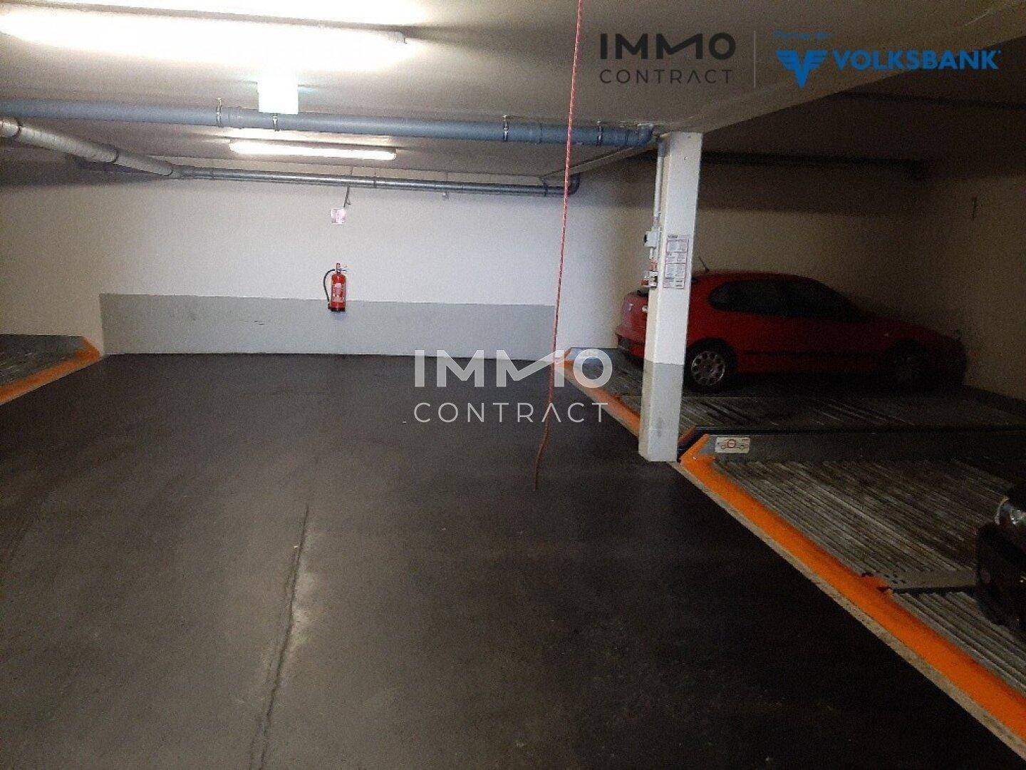 Geräumige Tiefgarage mit Betonboden, einem Parkliftsystem und einem Feuerlöscher an der Wand.