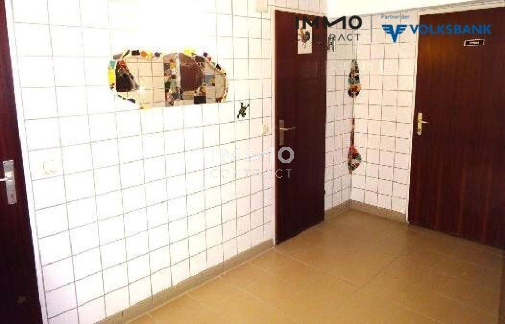 Gefliester Flur mit weißen Wandfliesen und zwei Holztüren, die zu weiteren Räumen führen.