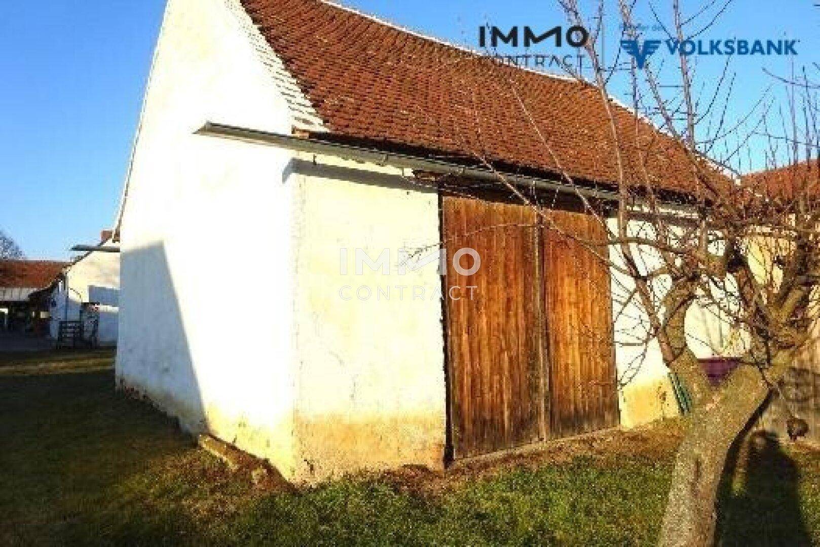 Altes Nebengebäude mit Holztüren und einem Ziegeldach, umgeben von Gras.