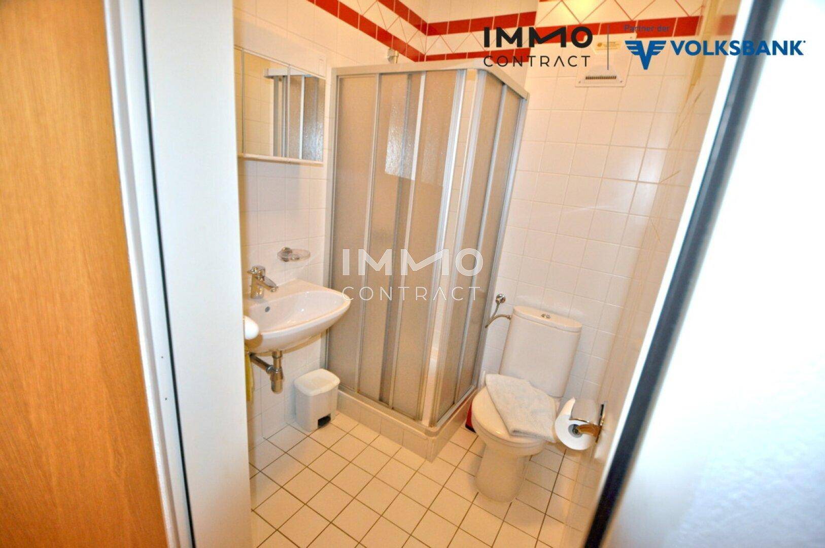 Funktionales Badezimmer mit Dusche, Waschbecken und WC, gefliest in Weiß und Rot.