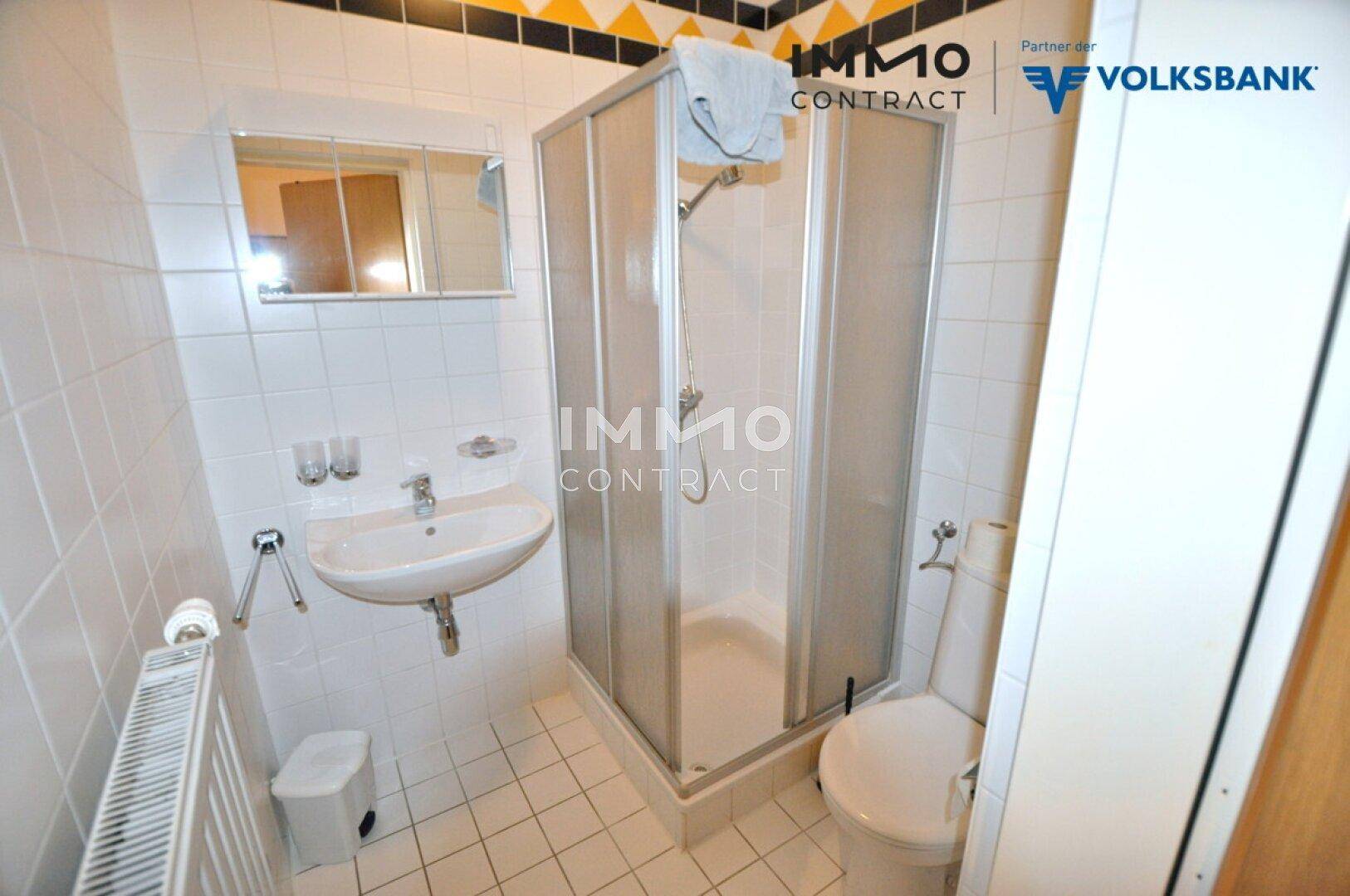 Kleines Badezimmer mit Dusche, Waschbecken und WC, komplett gefliest in Weiß und Gelb.