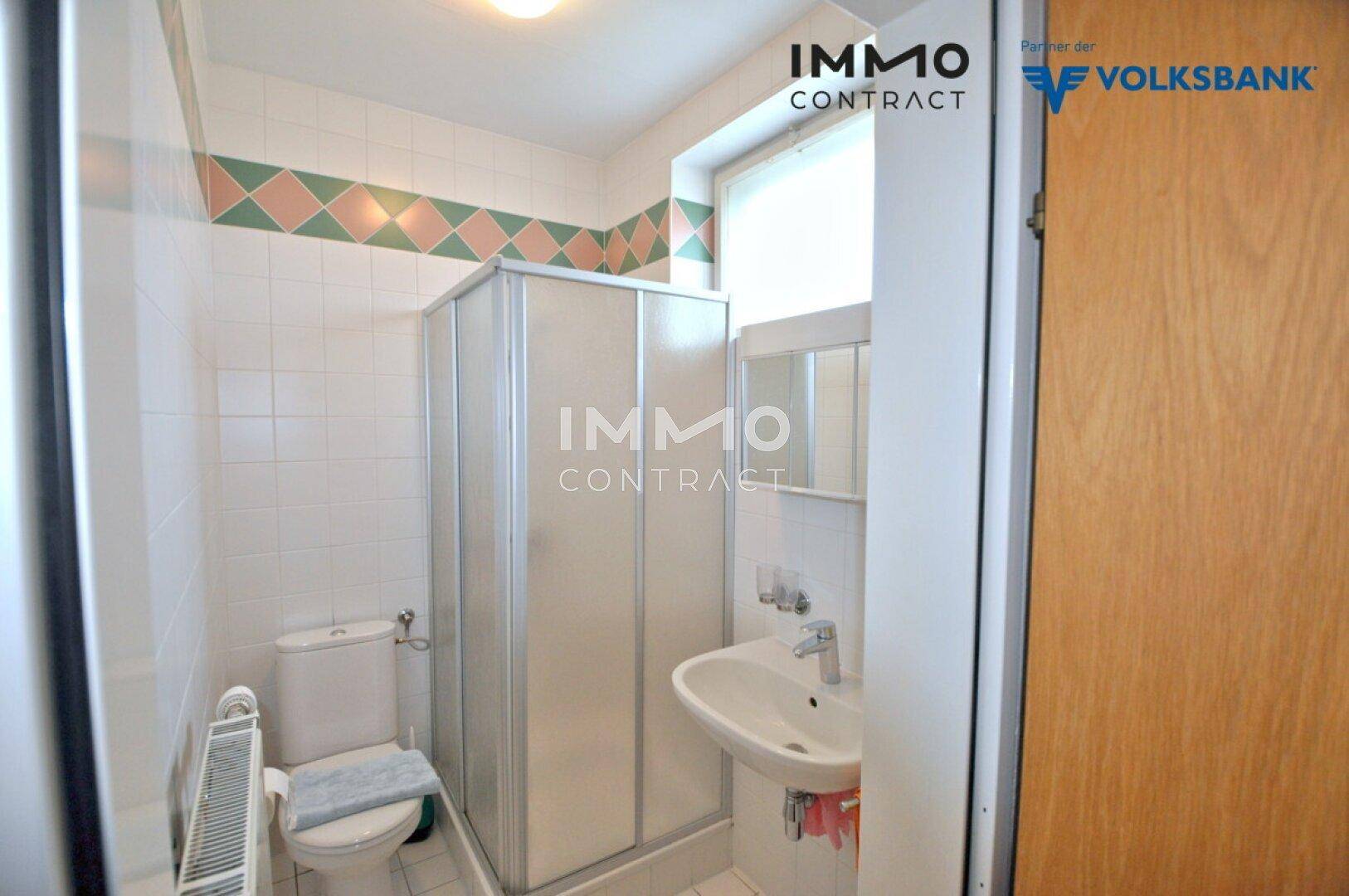 Helles Badezimmer mit Dusche, Waschbecken und WC, gefliest in Weiß, Grün und Rosa.