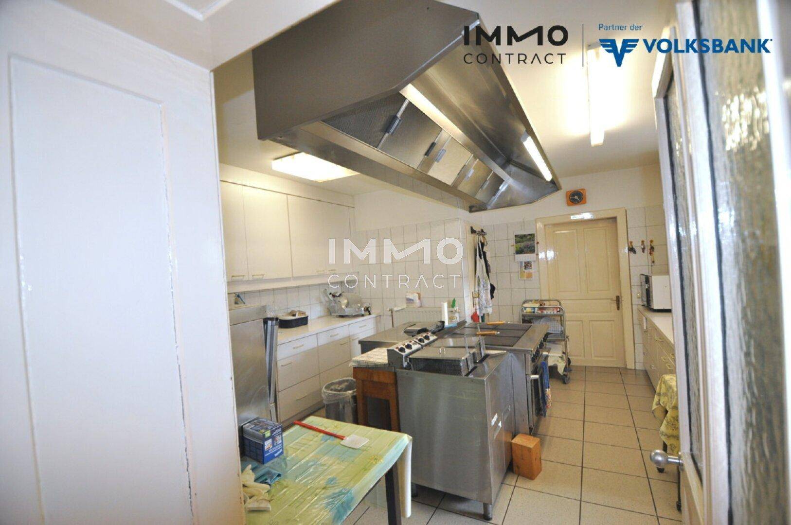 Professionelle Großküche mit Edelstahleinrichtungen, Dunstabzugshaube und Fliesenboden.