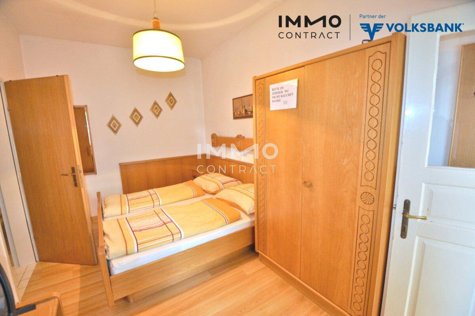 Helles Doppelzimmer mit zwei Einzelbetten, Holzschrank und einfacher Dekoration.