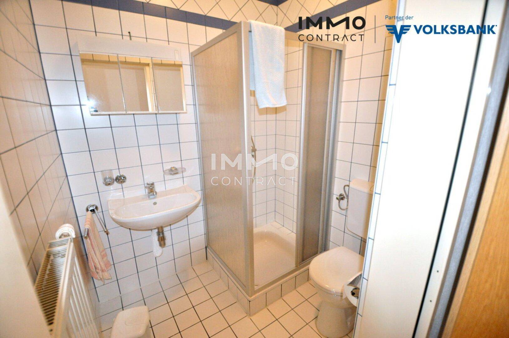 Kleines Badezimmer mit Dusche, Waschbecken und WC, komplett gefliest in Weiß und Blau.