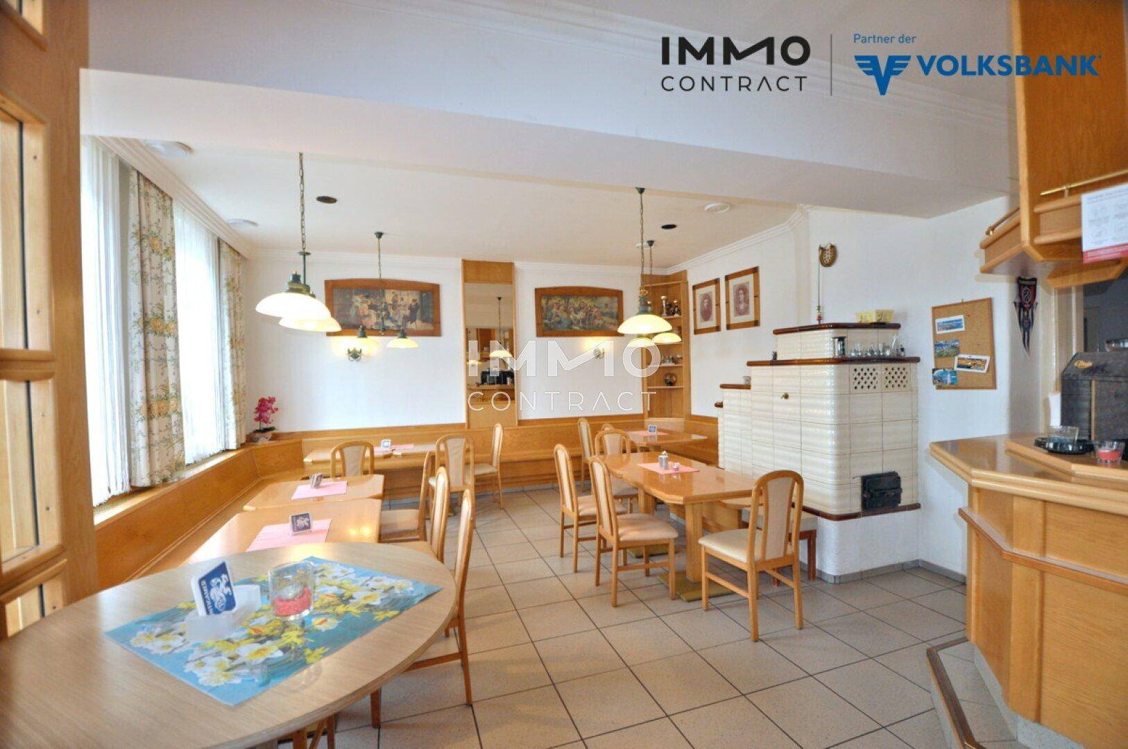 Heller Gastraum mit Holzeinrichtung, Fliesenboden und einem dekorativen Kachelofen.