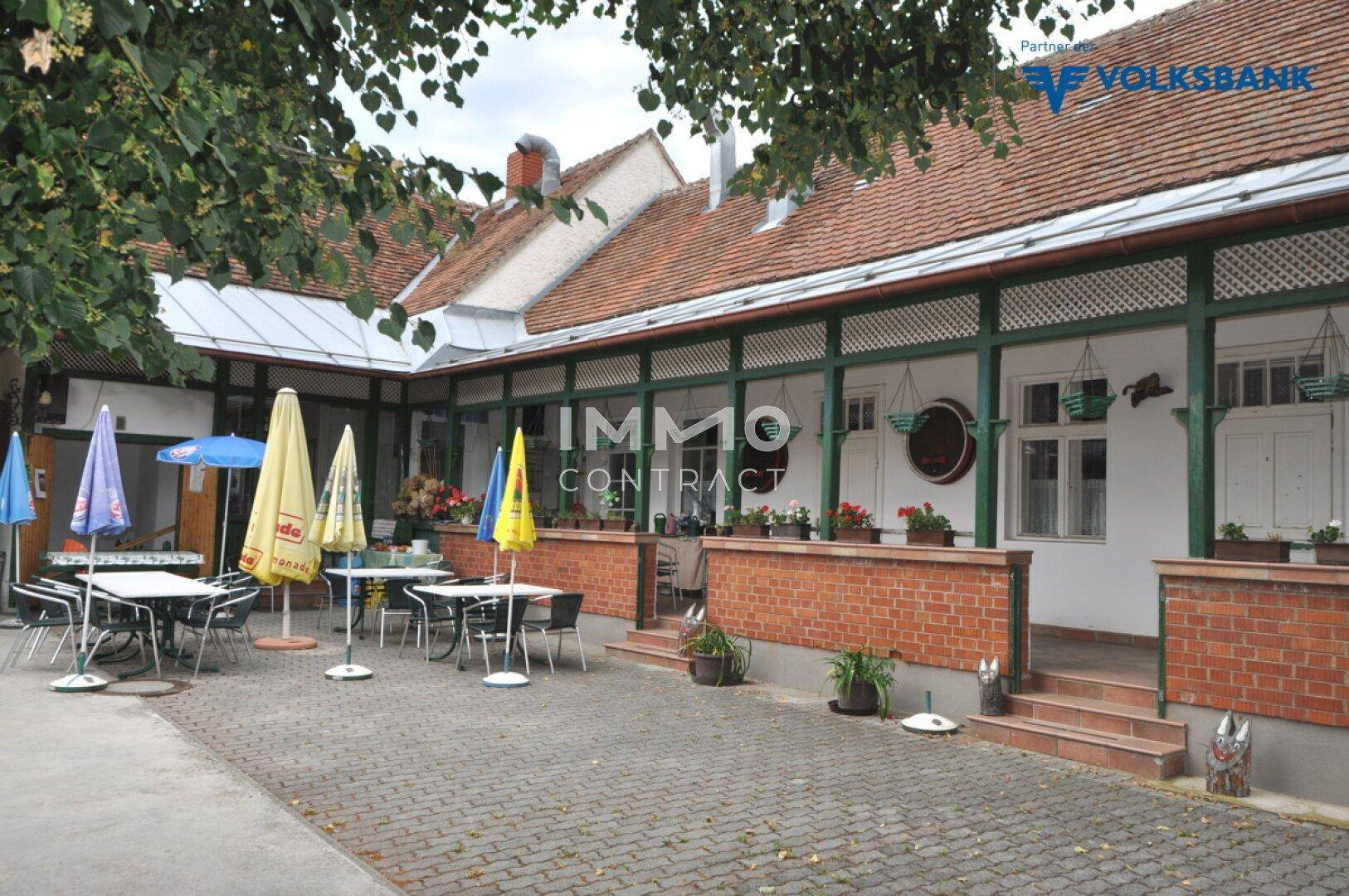 Großer gepflasterter Innenhof mit zahlreichen Tischen, Stühlen und Sonnenschirmen für Gäste.