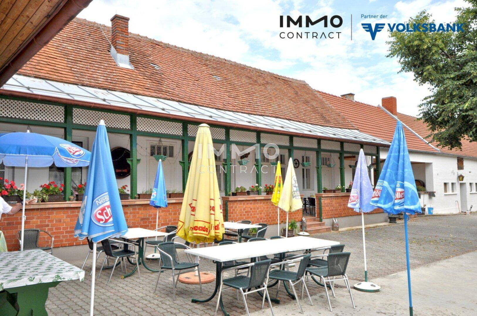 Weitläufiger Außenbereich mit vielen Sitzgelegenheiten und bunten Sonnenschirmen unter Bäumen.