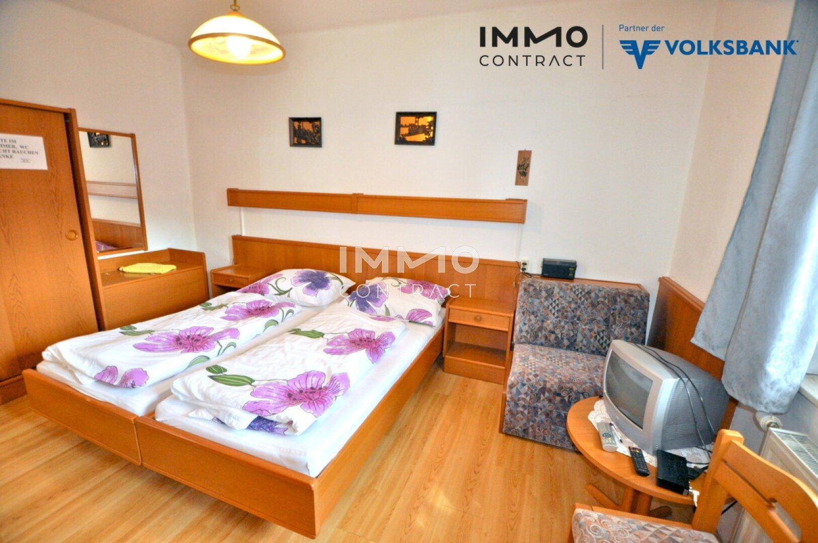 Geräumiges Doppelzimmer mit zwei Einzelbetten, Holzboden und einem kleinen Fernseher.