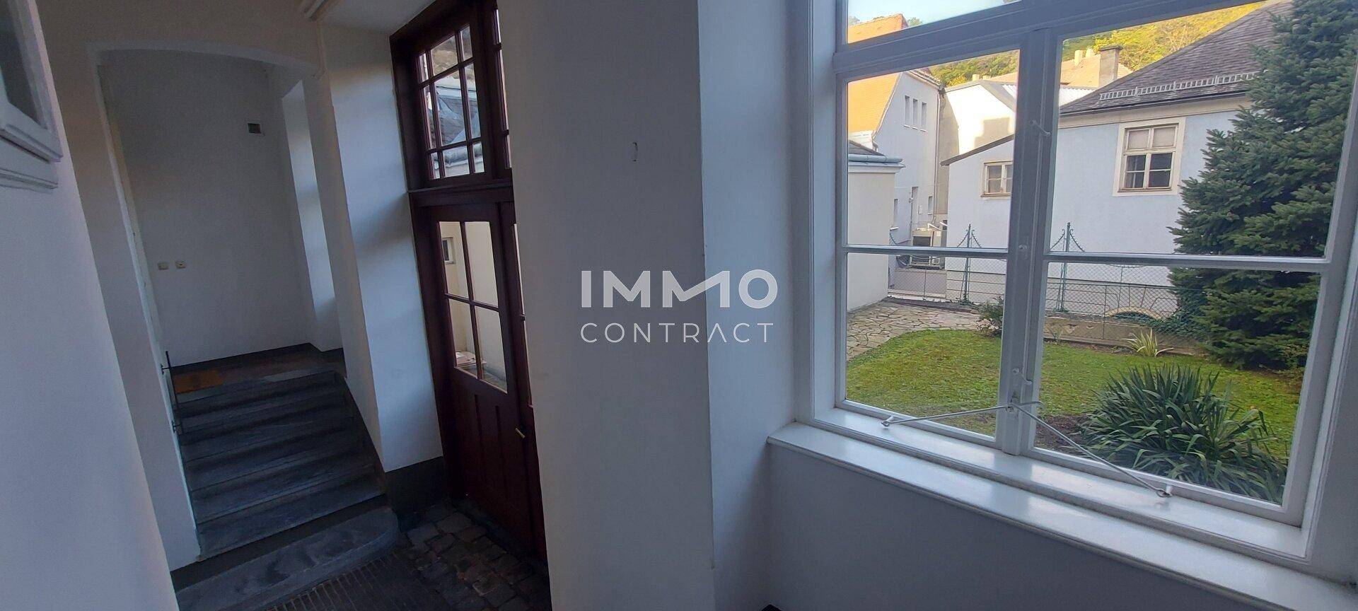 Heller Flur mit Blick auf einen grünen Innenhof und eine Treppe, die zu den oberen Etagen führt.