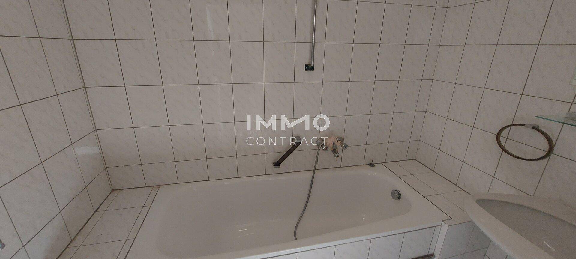 Badezimmer mit weißen Wand- und Bodenfliesen, ausgestattet mit einer Badewanne und Waschbecken.