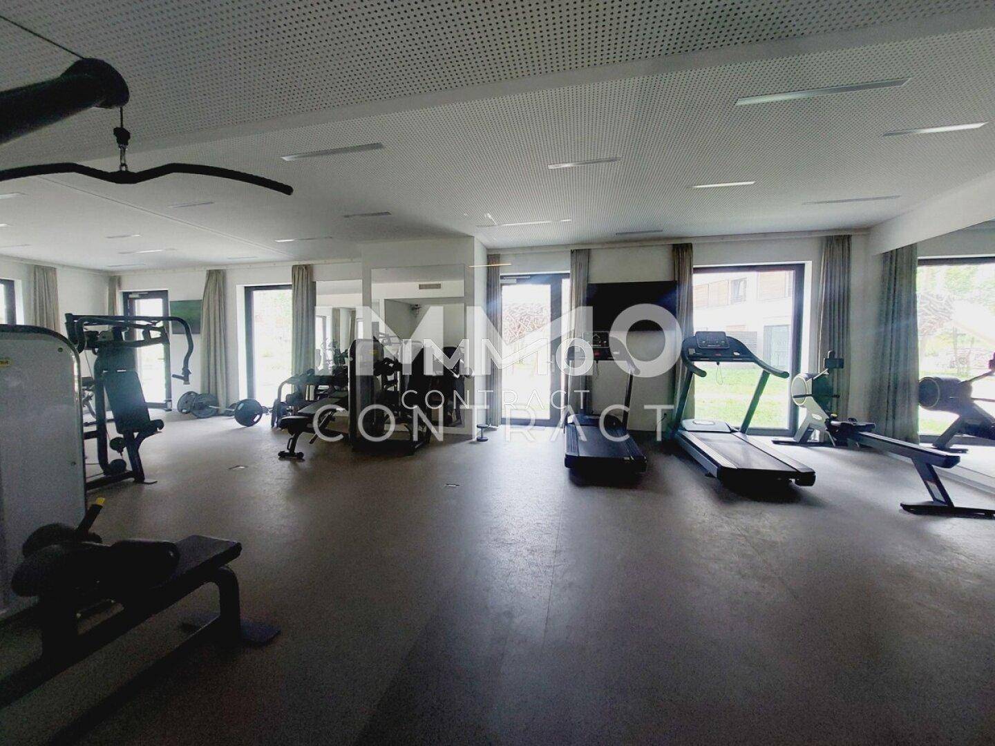 Gemeinschaftlicher Fitnessraum mit verschiedenen Trainingsgeräten und großen Fenstern.