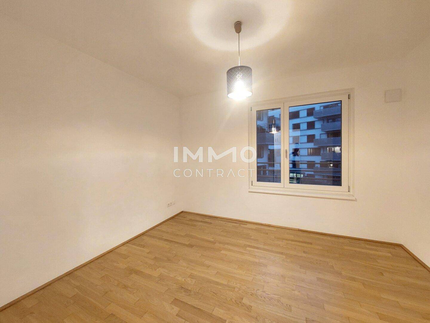 Schlafzimmer mit Parkettboden und großem Fenster, das viel Tageslicht hereinlässt.