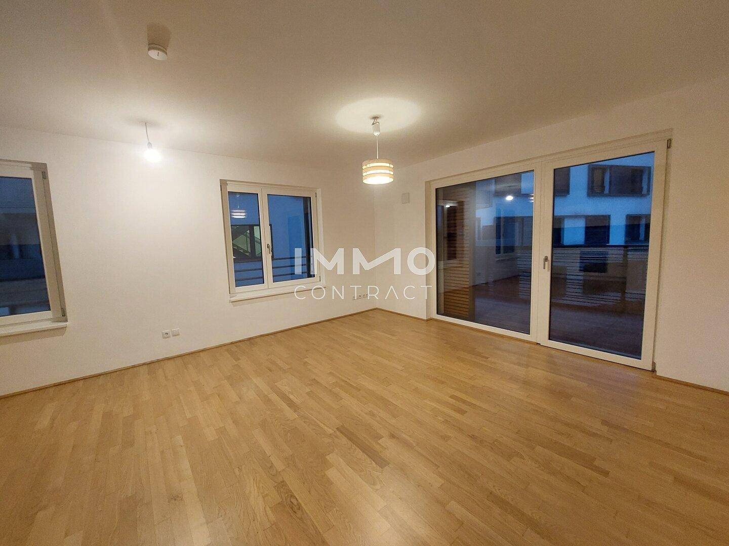 Geräumiges Wohnzimmer mit Parkettboden und Zugang zu einem Balkon oder einer Terrasse.