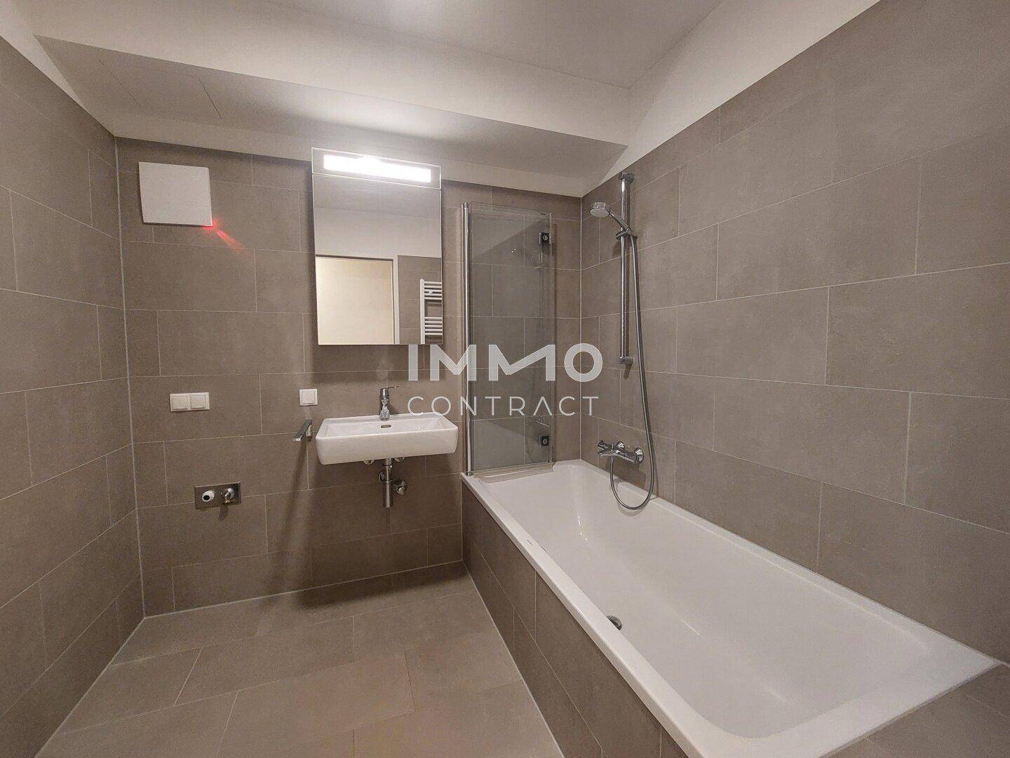 Modernes Badezimmer mit Badewanne, Waschbecken und grauen Fliesen an Wänden und Boden.