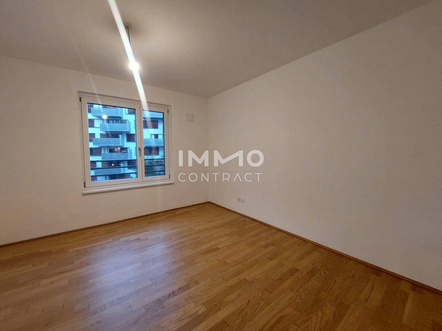 Helles Schlafzimmer mit Parkettboden und Blick auf die umliegenden Gebäude.