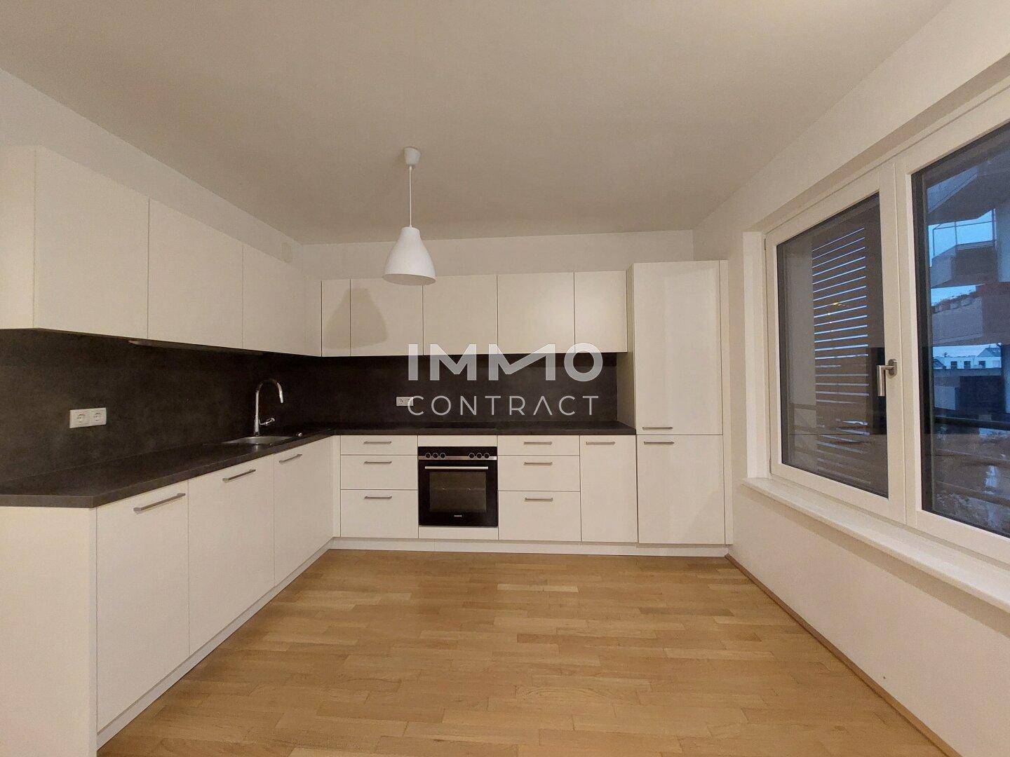 Moderne Einbauküche mit weißen Schränken, dunkler Arbeitsplatte und integriertem Backofen.