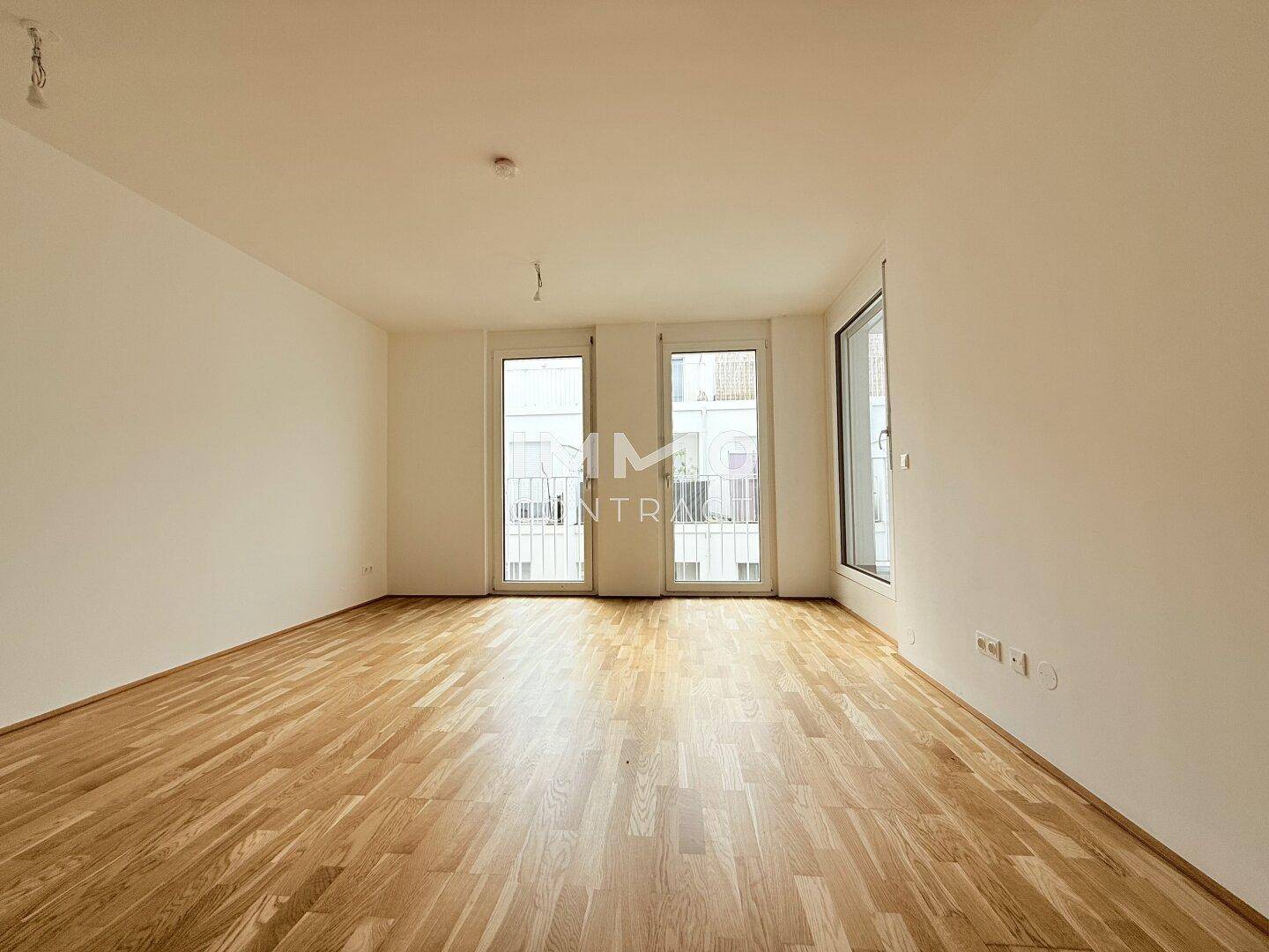 Heller, leerer Raum mit Parkettboden und Zugang zu einem französischen Balkon.