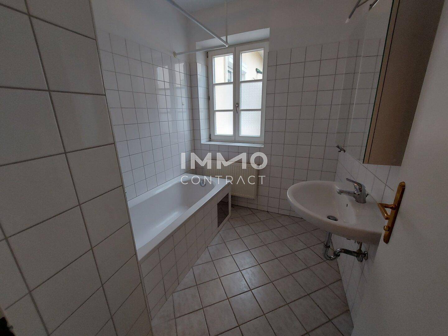 Badezimmer mit Badewanne, Waschbecken und Fenster, komplett gefliest in Weiß.