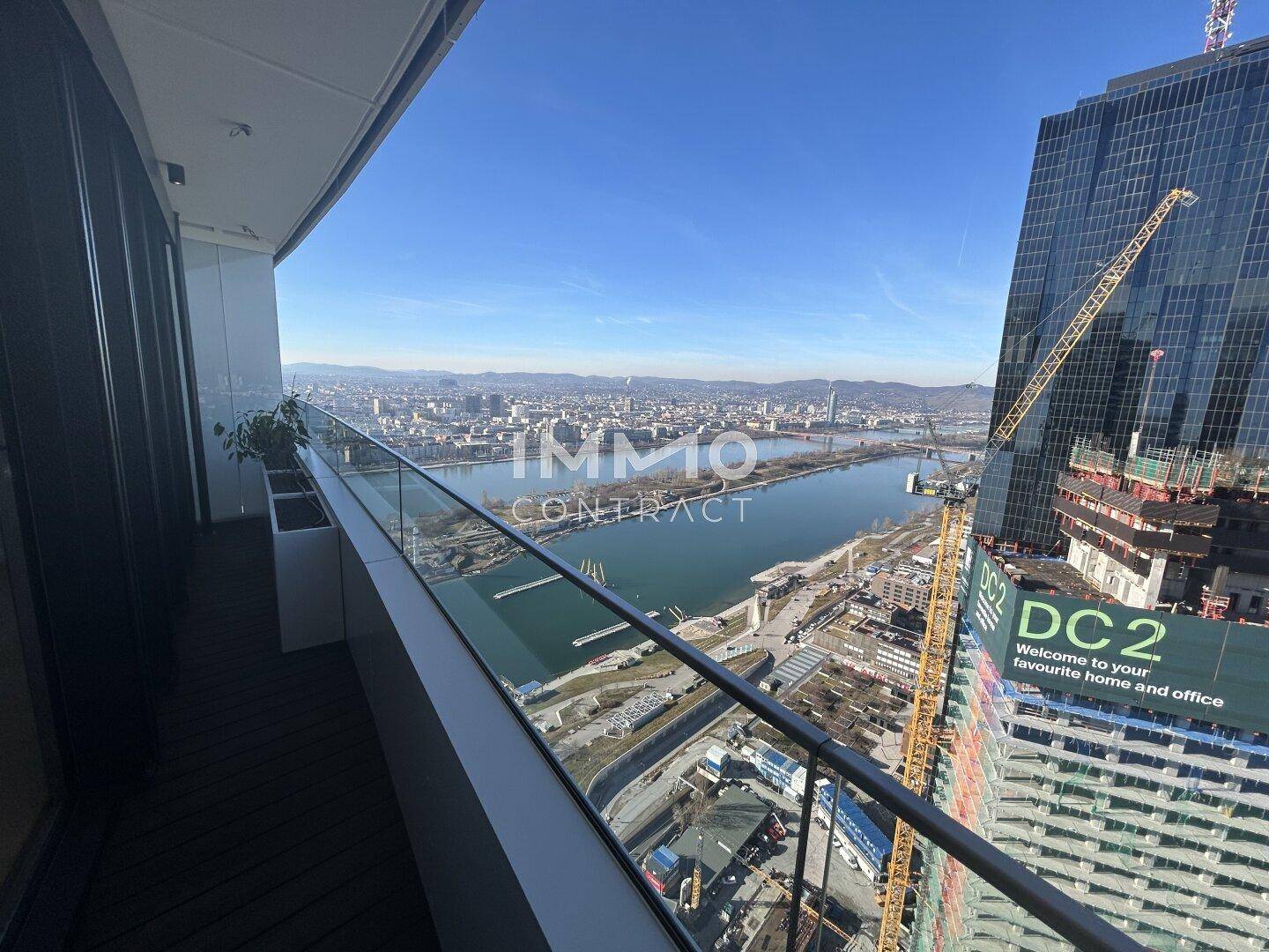Geräumiger Balkon mit Glasgeländer und Panoramablick auf die Stadt und den Fluss.