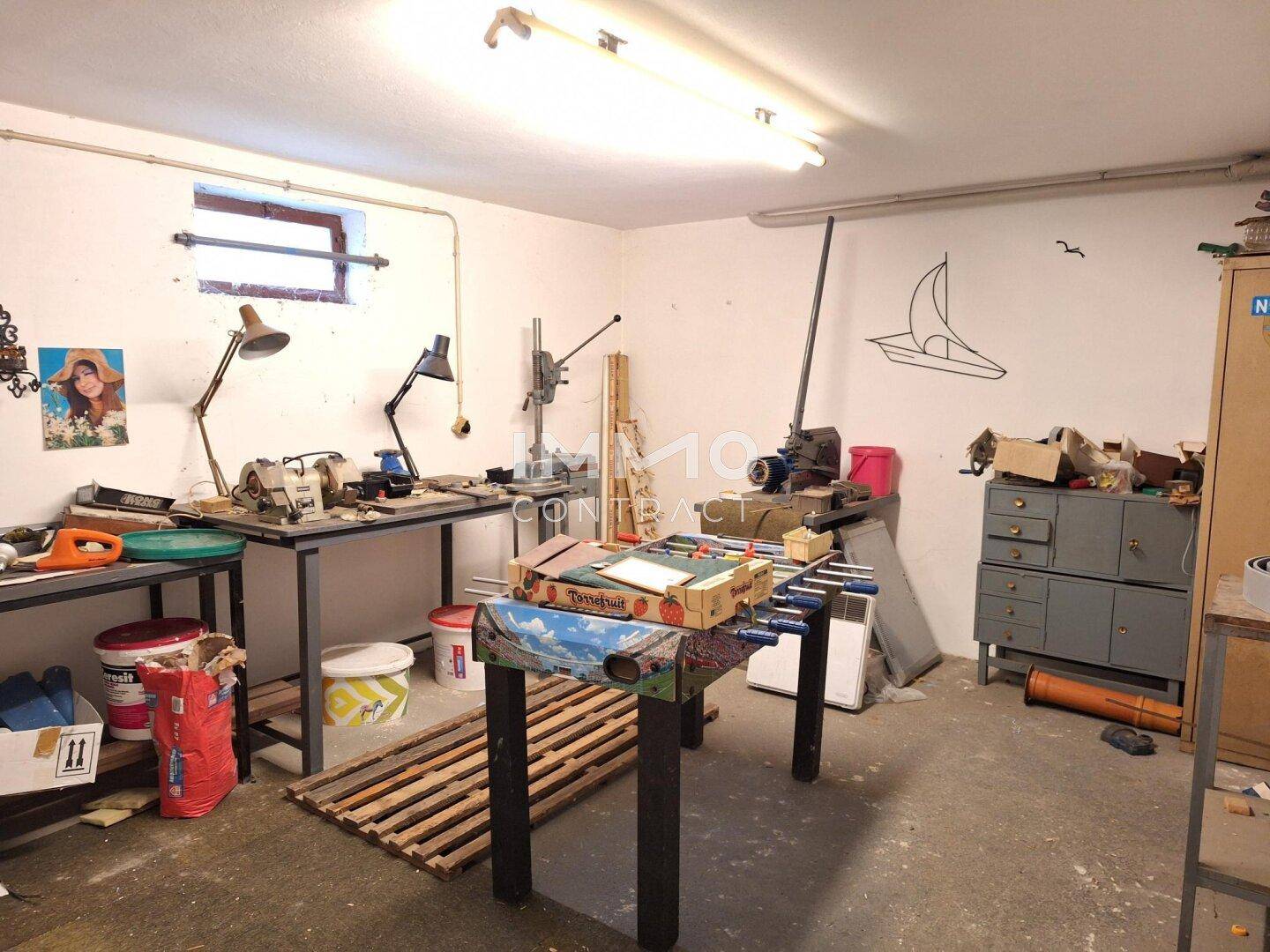 Werkstatt im Keller mit Arbeitstischen, Werkzeugen und einem Tischfußballspiel.