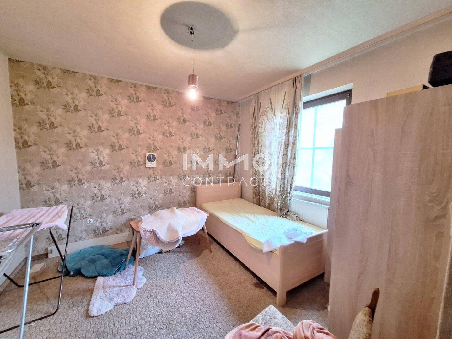 Einfaches Schlafzimmer mit gemusterter Tapete, Teppichboden und einem Einzelbett.