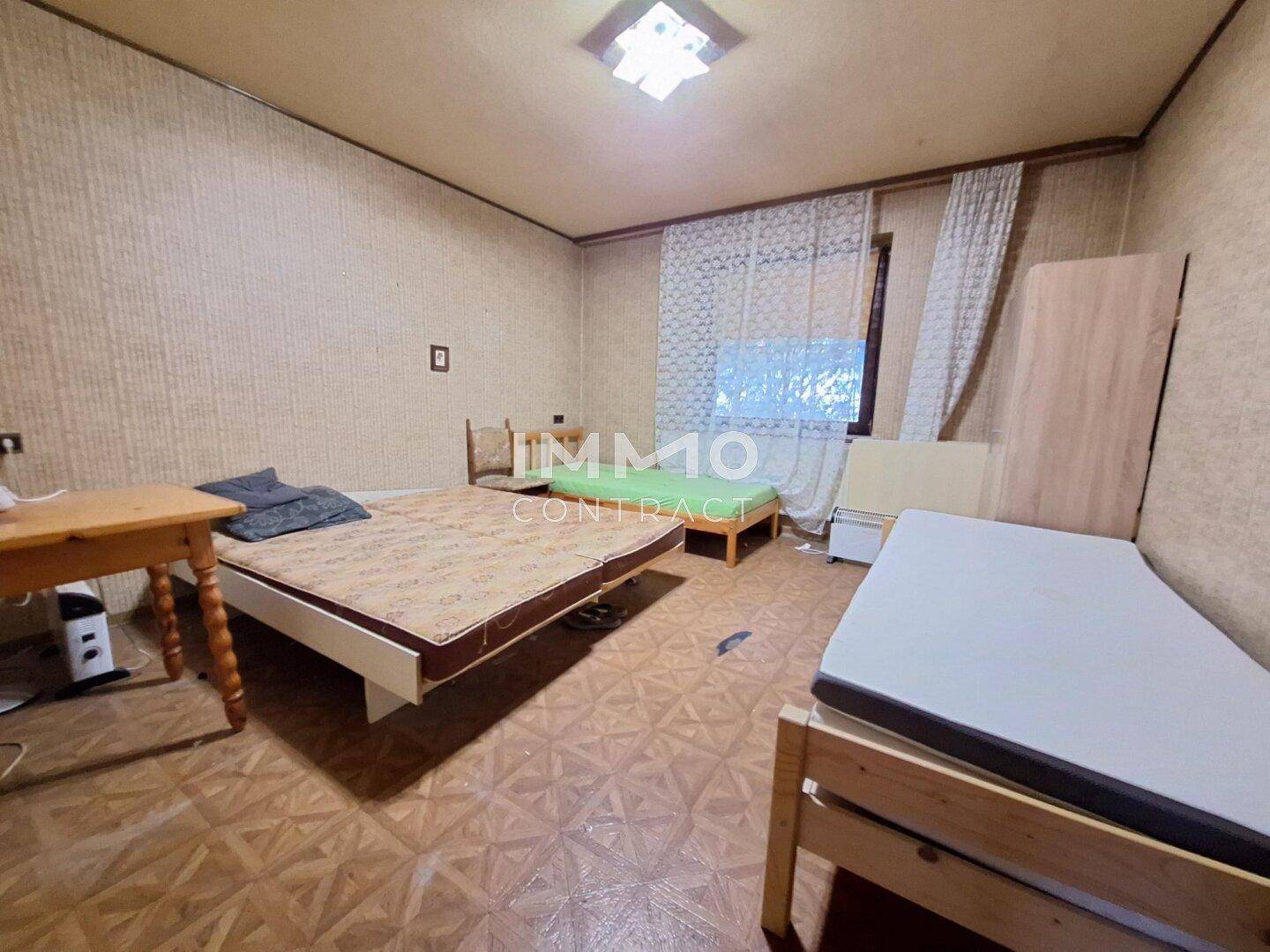 Schlafzimmer mit mehreren Betten, gemusterten Tapeten und einfacher Einrichtung.