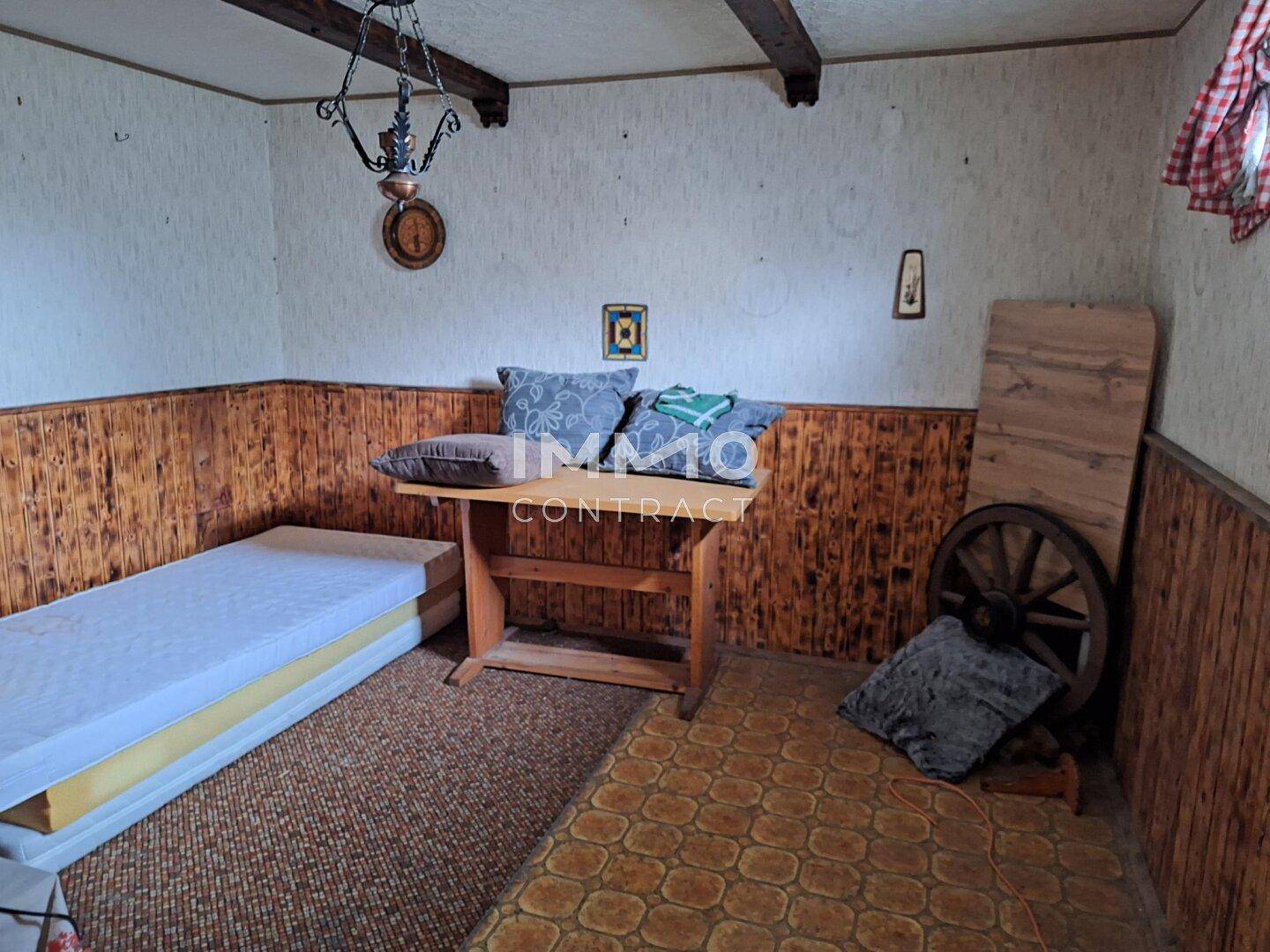 Rustikales Schlafzimmer mit Holzvertäfelung, gemusterter Tapete und einfacher Einrichtung.