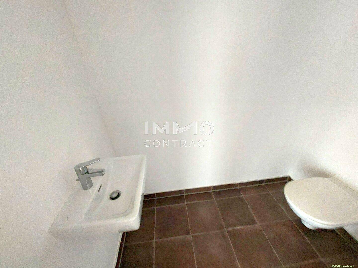Gäste-WC mit Toilette, kleinem Waschbecken und Fliesenboden.