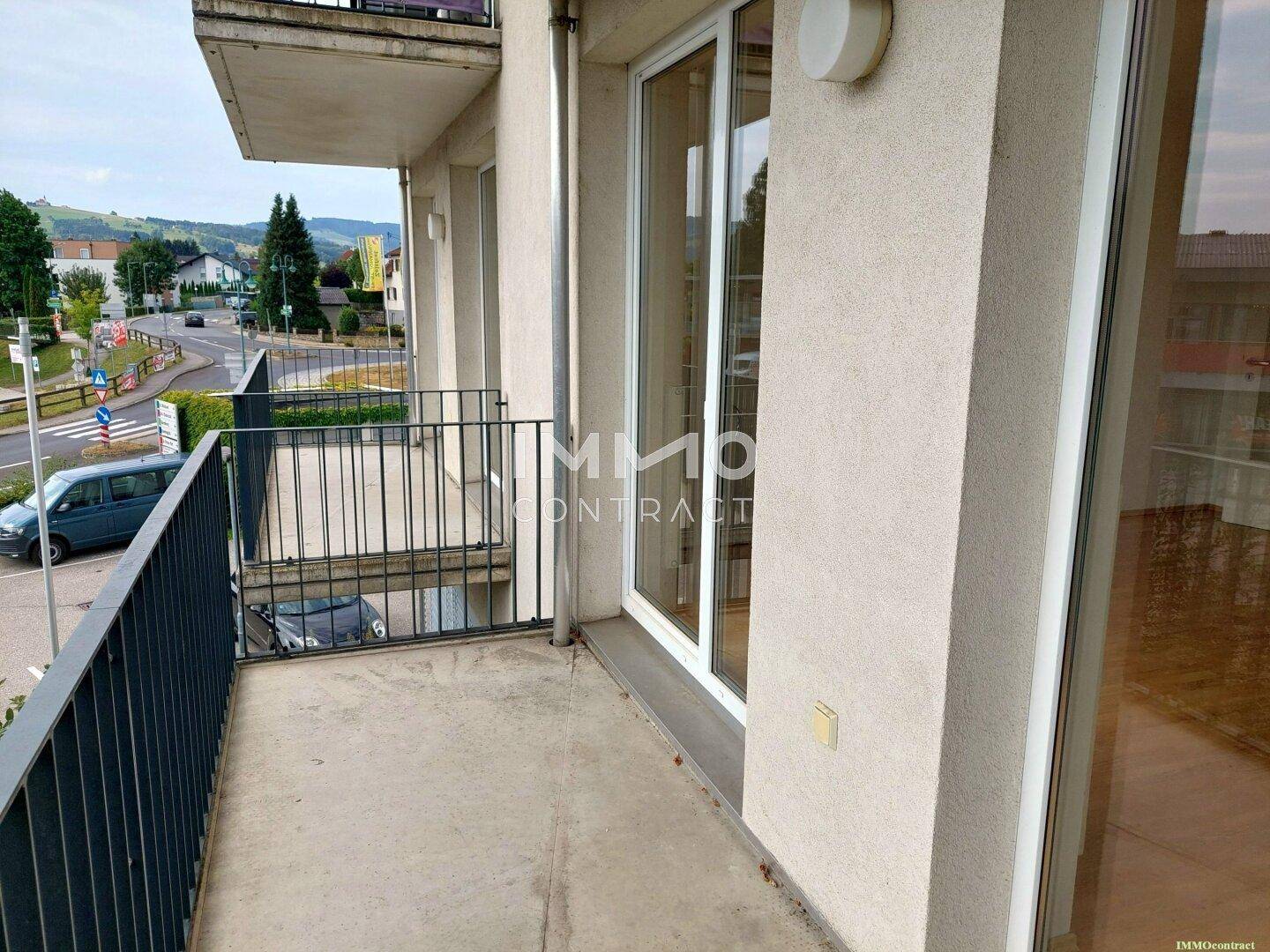 Geräumiger Balkon mit Metallgeländer und Ausblick auf die Umgebung und ferne Hügel.